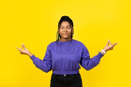Téléchargez les photos : Jeune femme méditant en pull violet avec les yeux fermés et les doigts zen isolés sur fond jaune. - en image libre de droit