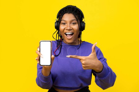 Photo for Woman showcasing a smartphone with a blank screen for advertising in purple sweater on a vibrant yellow background. - Royalty Free Image