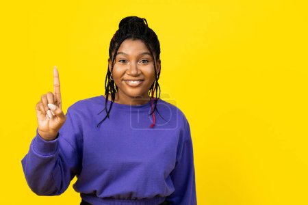 Téléchargez les photos : Afro femme pointant vers le haut sur un fond jaune vif, exprimant la positivité et les idées. - en image libre de droit