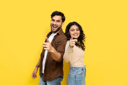Téléchargez les photos : Couple heureux pointant vers la caméra sur fond jaune - Concept de joie, de jeunesse et de convivialité - en image libre de droit
