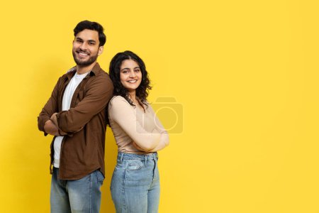 Téléchargez les photos : Joyeux couple debout dos à dos avec des sourires confiants, habillé avec désinvolture sur un fond jaune vibrant - en image libre de droit