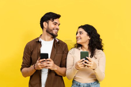 Téléchargez les photos : Jeune Couple Engrossed In Smartphones sur fond jaune, Communication, Médias sociaux - en image libre de droit