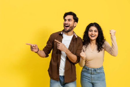 Foto de Emocionada pareja joven señalando y celebrando el éxito sobre fondo amarillo, emoción positiva, logro - Imagen libre de derechos