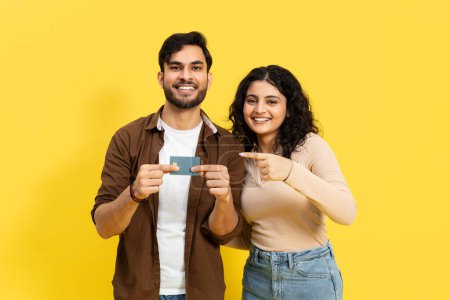 Téléchargez les photos : Happy Couple Affichage d'une carte de crédit sur fond jaune, e-commerce, achats en ligne, concept de finance - en image libre de droit