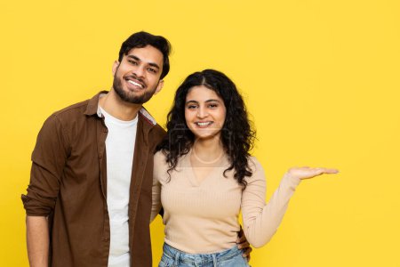 Photo for INDIAN COUPLE POINTING ON YELLOW BACKGROUND Showcasing Open Hand Gesture, Dynamic Duo With A Friendly And Welcoming Vibe - Royalty Free Image