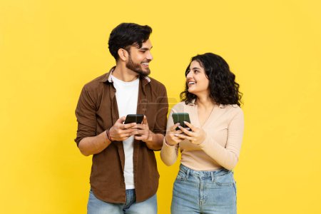 Téléchargez les photos : Happy Couple partageant du contenu sur Smartphones sur fond jaune, Communication en ligne, Médias sociaux, Style de vie technologique, Vêtements décontractés, Jeunes adultes, Sourire, Connectivité, Vibrant - en image libre de droit