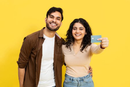 Téléchargez les photos : Happy Couple Affichage d'une carte de crédit sur fond jaune, sourire des jeunes adultes, concept de finance, achats en ligne, paiement - en image libre de droit