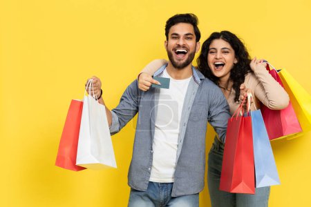 Foto de Pareja alegre con coloridas bolsas de compras y tarjeta de crédito en el fondo amarillo, excitado compras Spree, venta feliz - Imagen libre de derechos