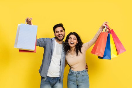 Foto de Feliz pareja de compras junto con coloridas bolsas contra el fondo amarillo - Imagen libre de derechos