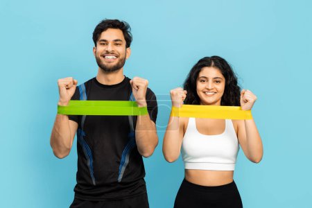 A Young Couple Smiling And Working Out Together Using Resistance Bands. Athletic Man And Woman Engaged In Strength Training On A Blue Background, Promoting A Healthy And Active Lifestyle.