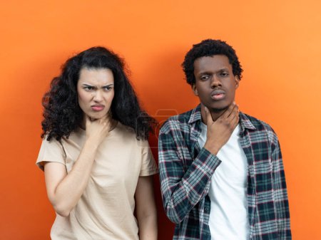SORE THROAT SYMPTOMS ILLUSTRATED BY DISTRESSED COUPLE: Young Man Touching Neck With Pain Expression And Woman Frowning In Discomfort, Health Issue Concept Against Orange Background