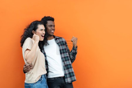 Photo for Excited Couple Success Achievement Celebration. Joyful Multiethnic Man And Woman Celebrate With Fist Pump Gesture. Cheerful Partners On Orange Background Show Happiness And Victory In Casual Outfits. - Royalty Free Image