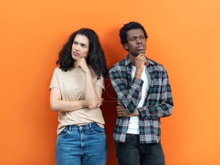 Photo for Thoughtful Couple With Pensive Expression Standing Against Orange Background, Decision Making, Doubt, Relationship Issues, Young Adults, Diverse Ethnicity, Casual Wear - Royalty Free Image