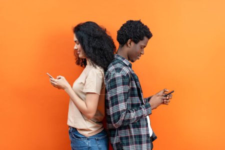 Téléchargez les photos : Connecté mais seul : deux jeunes adultes gravés dans les smartphones sur fond orange vibrant, représentant le concept des médias sociaux, de la communication et du mode de vie moderne. - en image libre de droit