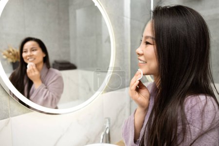 Téléchargez les photos : Femme en peignoir regardant reflet dans le miroir rond moderne dans le cadre de la salle de bains. Cozy Home Lifestyle et design d'intérieur élégant Concept. Routine matinale. - en image libre de droit