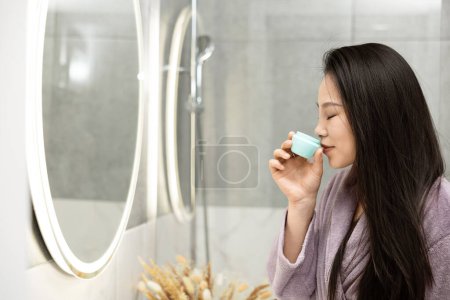 Téléchargez les photos : Routine du matin dans la salle de bain moderne, femme tenant produit de soins de la peau - en image libre de droit