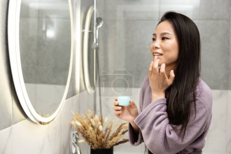 Téléchargez les photos : Femme en peignoir appliquant la crème pour la routine quotidienne de beauté - en image libre de droit