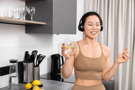 Foto de Mujer joven disfrutando de la música en la cocina con agua de limón saludable - Imagen libre de derechos