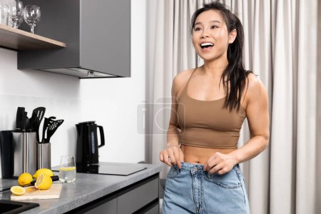 Mujer joven feliz en desgaste casual en el interior de la cocina moderna que muestra la pérdida de peso. Vida Saludable, Alegría, y Concepto de Bienestar. Resultados de alta energía, emociones positivas y dieta.