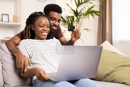 Téléchargez les photos : Couple affectueux engagés dans des achats en ligne, en utilisant une carte de crédit et un ordinateur portable tout en étant assis confortablement sur un canapé à la maison. - en image libre de droit