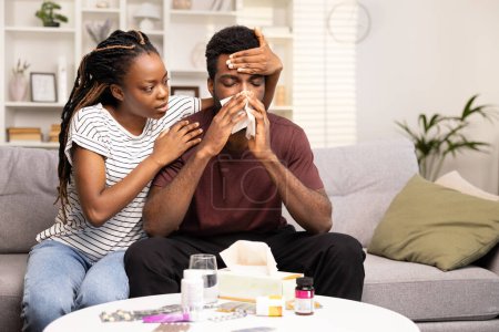 Téléchargez les photos : Femme bienveillante réconfortant l'homme malade à la maison avec des symptômes de grippe, entouré de médicaments et de tissus sur le canapé, les soins de santé et le concept de soutien - en image libre de droit