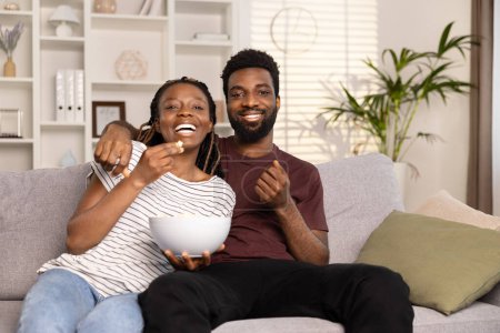 Photo for Happy Couple Relaxing On Couch At Home Enjoying Movie With Popcorn. Cozy Domestic Lifestyle And Togetherness Concept. - Royalty Free Image