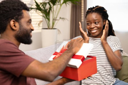 Photo for Surprise Gift Exchange Between Happy Couple At Home. Joyful Woman Receiving Red Box Present From Man. Happiness, Love, And Togetherness Concept For Special Occasion Or Holiday. - Royalty Free Image