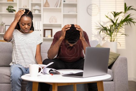 Gestresstes junges Paar verwaltet Finanzen, schaut auf Laptop und Dokumente, zeigt Sorge und Besorgnis, Home Interior