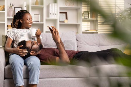Foto de Pareja relajada en casa, Mujer con café abrazando al hombre en el sofá, comodidad casual, acogedor interior de la sala de estar - Imagen libre de derechos