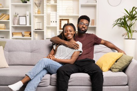Téléchargez les photos : Couple affectueux câlins sur le canapé à la maison, rayonnant d'amour, de confort et de convivialité dans un cadre confortable salon - en image libre de droit