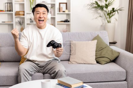Photo for Man Winning at Video Games on Couch at Home. Excited male gamer is celebrating a victory while playing a console game, showing emotions of euphoria and happiness in a cozy living room setting. - Royalty Free Image