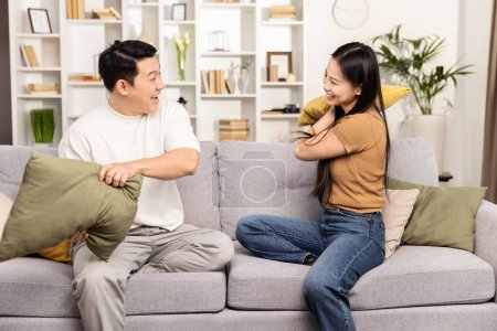 Photo for An exuberant couple enjoys a playful pillow fight on their couch, laughing and sharing a lighthearted moment together in a cozy living room. - Royalty Free Image