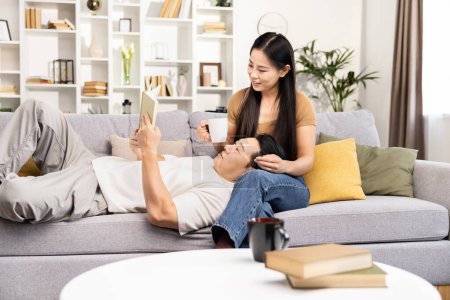 Entspanntes Paar zu Hause, Mann liest Buch im Liegen auf dem Schoß der Frau, gemütliche Wohnzimmeratmosphäre, gemeinsame Freizeit
