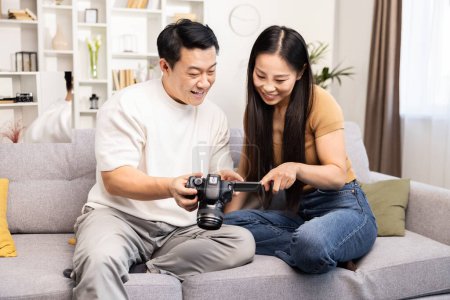 Photo for A joyful couple sits on the sofa, reviewing photos on a digital camera, sharing a light-hearted moment in a cozy home setting. - Royalty Free Image
