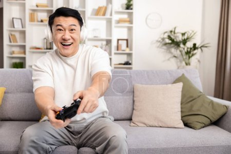 Erwachsener Mann, der zu Hause Videospiele spielt, aufgeregter Gamer mit Kopfhörern auf der Couch, Genuss, Freizeit, Spieltechnologie-Konzept