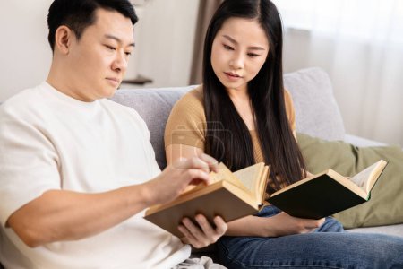 Couple Reading Books Together On Sofa, Serene Home Leeisure, Quality Time, Educational Activity, Relaxed Atmosphere, Adult Education, Casual Enjoyment, Asian Couple Leisure Time, Reading Session. 