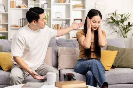 Konfliktlösung in der Beziehung: Ein Mann versucht zu reden, eine Frau ist aufgebracht und verdeckt ihre Ohren, um Gespräche in einem modernen Wohnzimmer zu vermeiden