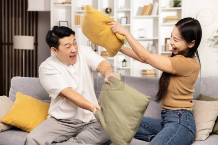 Photo for A joyful couple engages in a playful pillow fight on their cozy couch in a well-lit living room, sharing a fun, carefree moment together. - Royalty Free Image