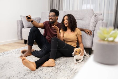 Téléchargez les photos : Couple se détendre sur le sol avec chien regarder la télévision dans le salon moderne - en image libre de droit