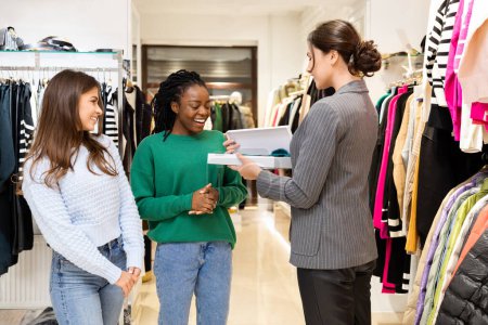 Photo for Happy Customers Shopping In Clothing Store With Assistant Handing Box with Good, Diverse Women Enjoying Fashion Shopping, Retail Experience - Royalty Free Image
