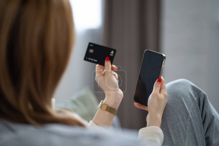 Foto de Experiencia de compras en línea: Mujer sosteniendo la tarjeta de crédito y el teléfono inteligente, centrado en la transacción de comercio electrónico en el entorno del hogar moderno - Imagen libre de derechos