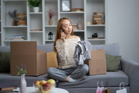 Photo for Young Woman Enjoying Unboxing Shopping Finds At Home, Expressing Joy And Satisfaction While Talking On The Phone, Trendy Indoor Setting - Royalty Free Image