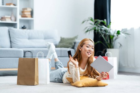Photo for Young Woman Enjoying Online Shopping From Home, Smiling at Smartphone While Surrounded by Shopping Bags and Holding Tablet. - Royalty Free Image