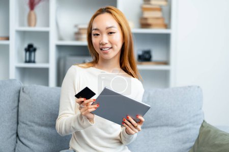 Téléchargez les photos : Jeune femme heureuse utilisant la tablette et tenant la carte de crédit sur le canapé, achats en ligne, mode de vie moderne - en image libre de droit