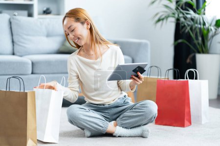 Happy Woman Shopping en ligne à la maison, profiter du commerce électronique avec tablette et sacs, style de vie décontracté, confort et concept d'e-shopping