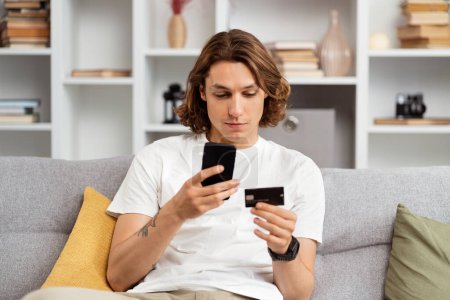 Junger Mann shoppt zu Hause online mit Kreditkarte und Smartphone, bequemem Casual Lifestyle und E-Commerce-Konzept