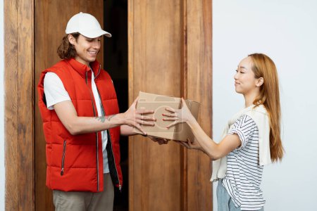 Entrega amistosa: Mensajero feliz en chaleco rojo que entrega el paquete a la mujer sonriente en casa. Servicio, Eficiencia, Compras Online.