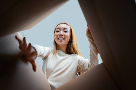 Photo for Happy Woman Unpacking Boxes In New Home, Excitement And Relocation Concept Captured From An Interesting Lower Perspective, Emphasizing Joy And New Beginnings. - Royalty Free Image