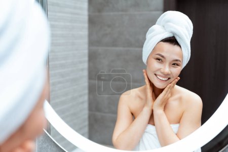 Photo for Young Woman In Bathroom With Towel On Head Smiling In Front Of Mirror, Exuding Happiness And Confidence, Perfect For Beauty And Self-Care Themes - Royalty Free Image