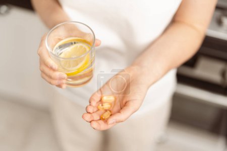 Nahaufnahme einer Frau, die ein Glas mit Zitronenwasser und Omega-3 in der Hand hält und sich auf die tägliche Gesundheit und Ernährung konzentriert, Wellness-Konzept
